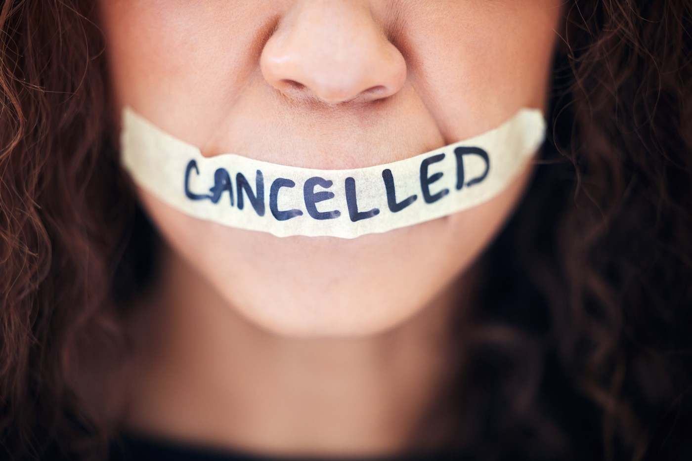 Closeup shot of an unrecognisable woman with tape on her mouth that has the word “cancelled” written on it
