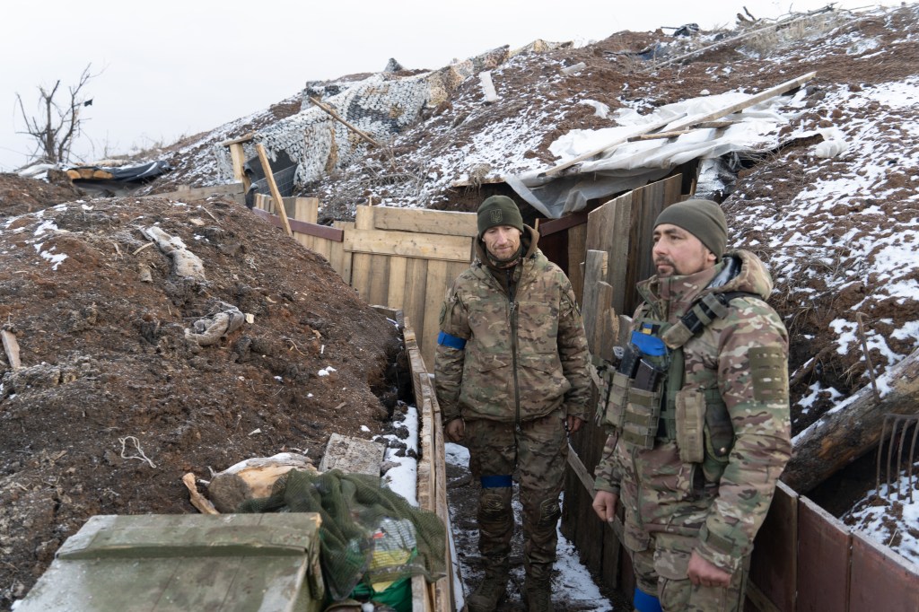 Two Ukrainian soldiers stand in a trench at the zero line south of the Russian-occupied city of Bakhmut. The top of the hill behind them marks the beginning of no man's land. (Photo via Bennett Murray)
