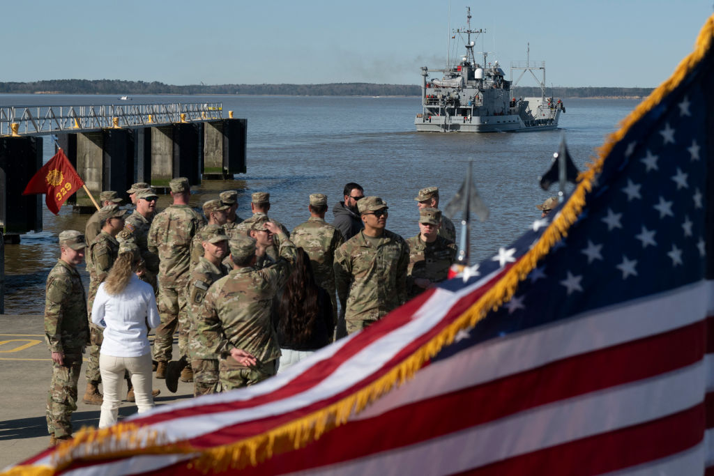 U.S. Army soldiers stand near a flag as the USAV Wilson Wharf sails away from the pier of the Joint Base Langley-Eustis during a media preview of the 7th Transportation Brigade deployment in Hampton, Virginia, on March 12, 2024. (Photo by ROBERTO SCHMIDT/AFP via Getty Images)