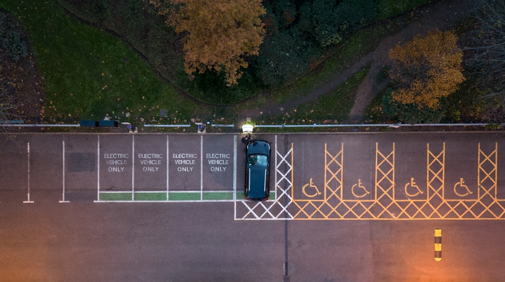 Overhead aerial view of a person connecting an electric car to an electrical vehicle charging station at dusk. (via Getty Images)
