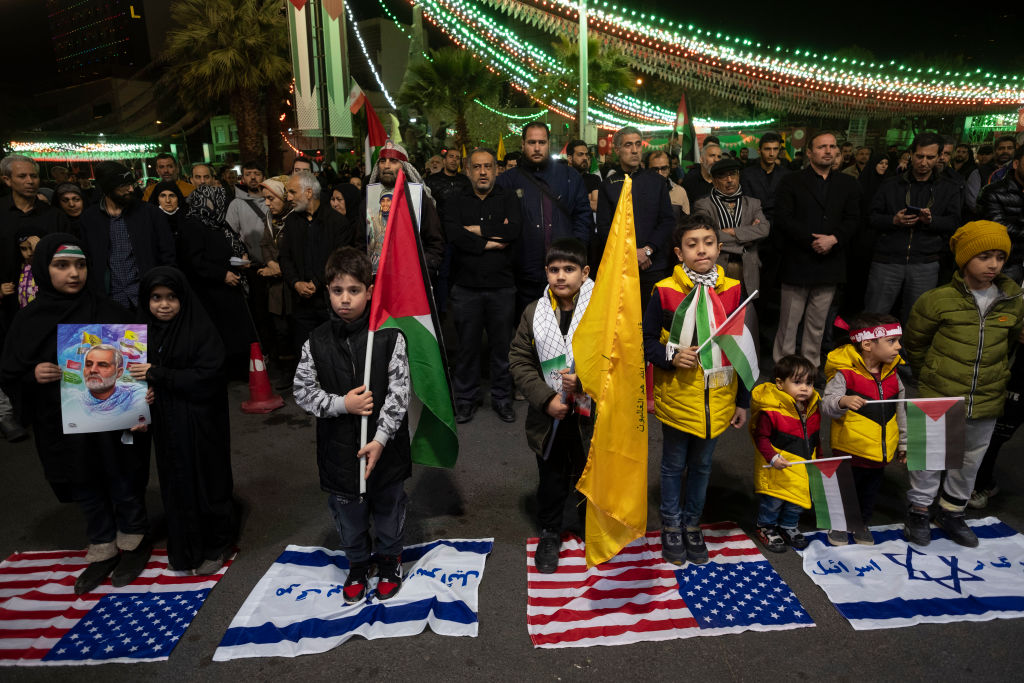 Young Iranian boys stand on U.S. and Israeli flags while carrying Palestinian flags and a portrait of the late commander of the Islamic Revolutionary Guard Corps' (IRGC) Quds Force, General Qassem Suleimani, during a protest in Tehran, Iran, on April 1, 2024. (Photo by Morteza Nikoubazl/NurPhoto via Getty Images)