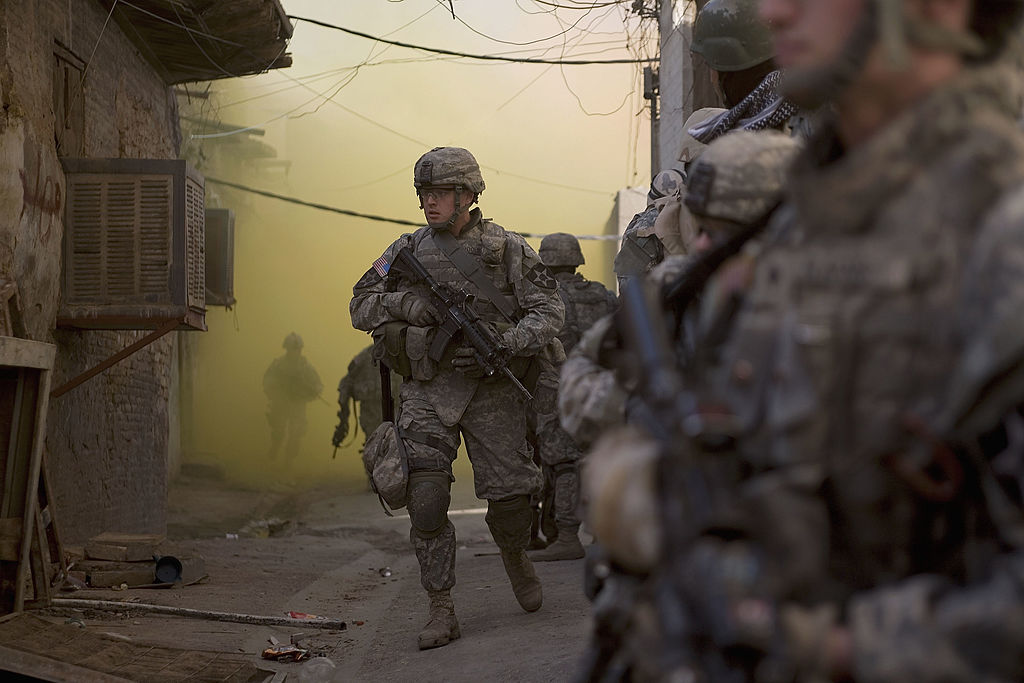 In an effort to disrupt Sunni insurgents and Shia militias in Baghdad, Iraq, U.S. Army soldiers from the Stryker Brigade combat team and Iraqi Army soldiers take cover with the aid of smoke grenades in January 2007. (Photo by Robert Nickelsberg/Getty Images)