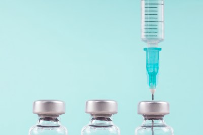 Row of medical vials and syringe. Glass bottles with a transparent potion on a light background