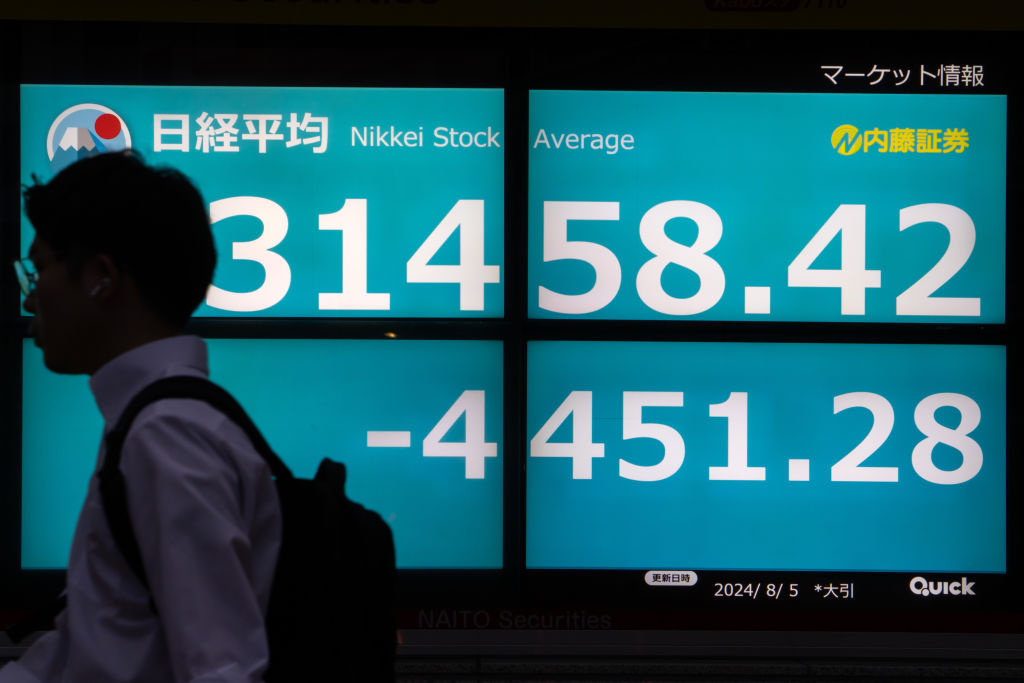 A pedestrian walks past monitors displaying the Nikkei 225 Stock Average figure outside a securities firm in Tokyo, Japan, on August 5, 2024. (Photo by Tomohiro Ohsumi/Getty Images)