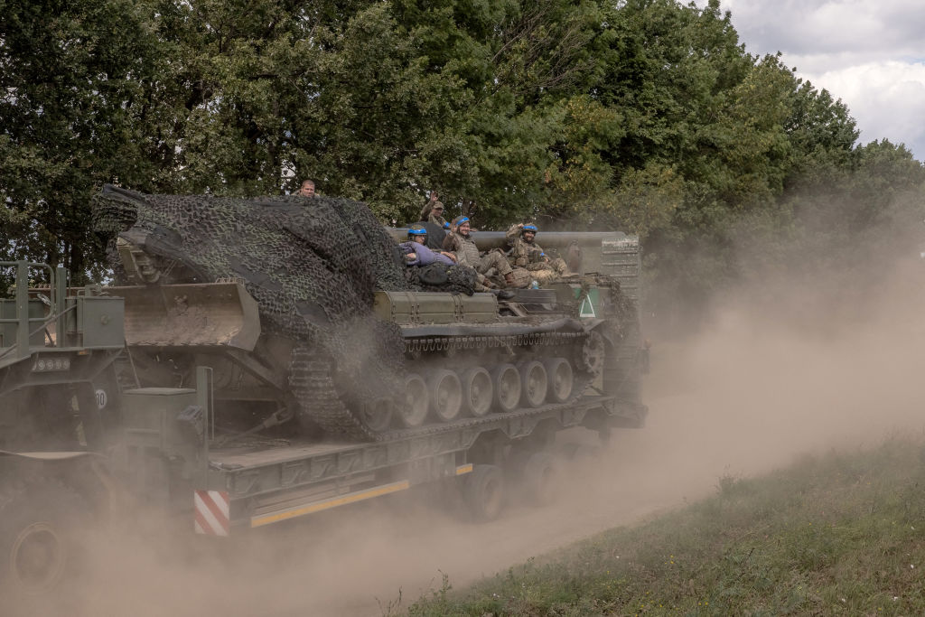 Ukrainian troops sit on a self-propelled artillery 2S7 Pion while being carried by a military truck, in the Sumy region, near the border with Russia, on August 11, 2024. (Photo by ROMAN PILIPEY/AFP via Getty Images)