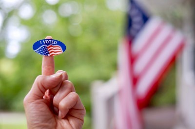 Finger holding up an I Voted sticker.