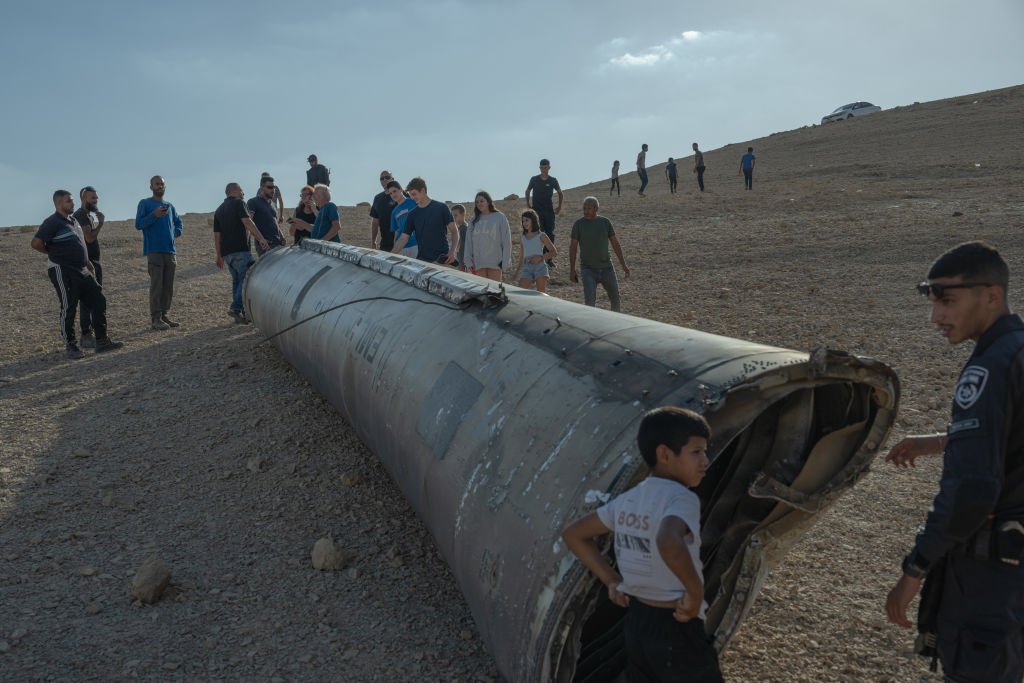 A group of people stand near the remains of a missile on October 2, 2024, near the Dead Sea, Israel, following a missile strike by Iran. (Photo by Erik Marmor/Getty Images)