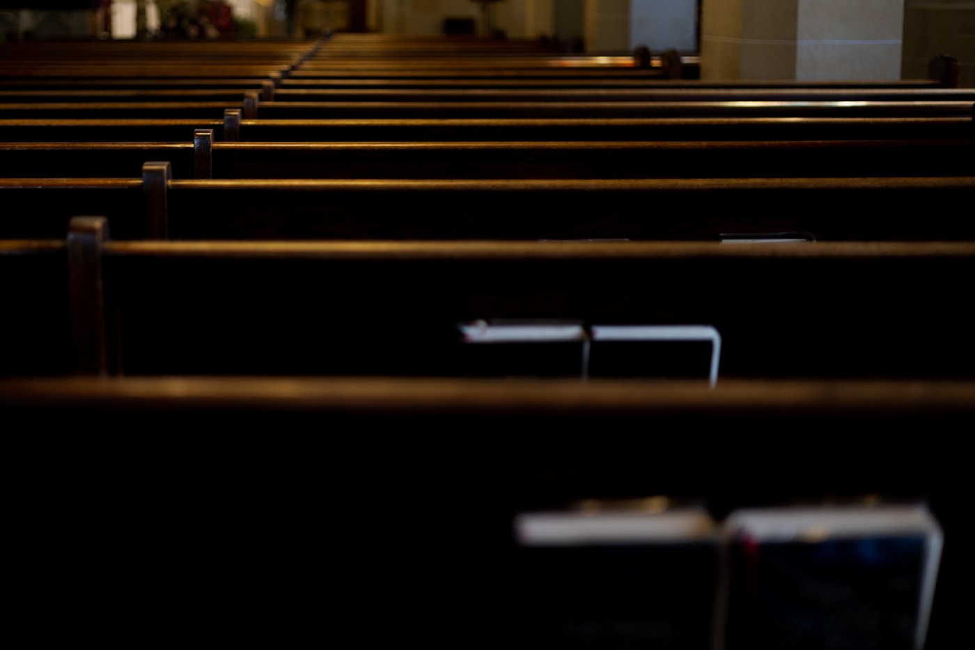 intersection of religion & politics: rear view of rows of wooden pews with religious liturgy books stored in pew racks in church