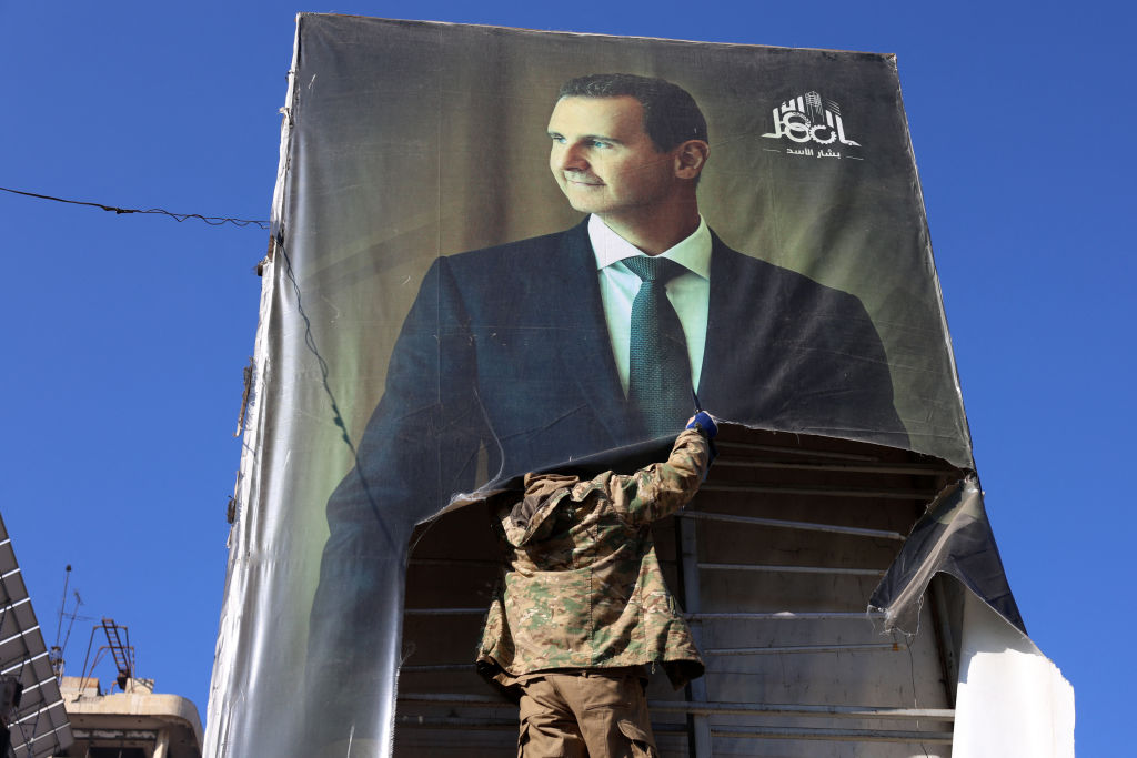 An anti-government fighter tears down a portrait of Syria's President Bashar al-Assad in Aleppo after rebels and their allies entered the northern Syrian city on November 30, 2024. (Photo by MOHAMMED AL-RIFAI/AFP via Getty Images)