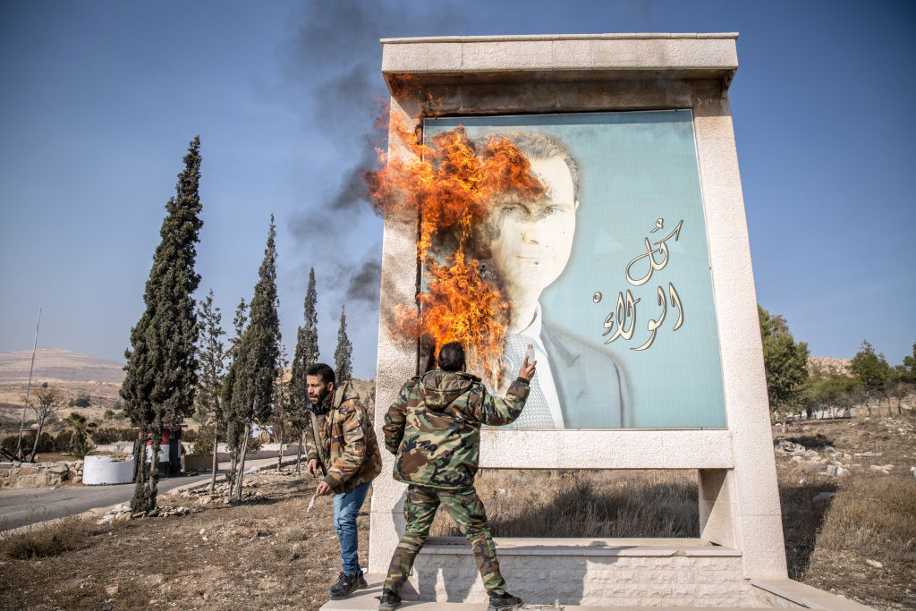 A man burns a picture of former Syrian President Bashar al-Assad close to Syria's border with Lebanon. (Photo by Sally Hayden/SOPA Images/LightRocket via Getty Images)