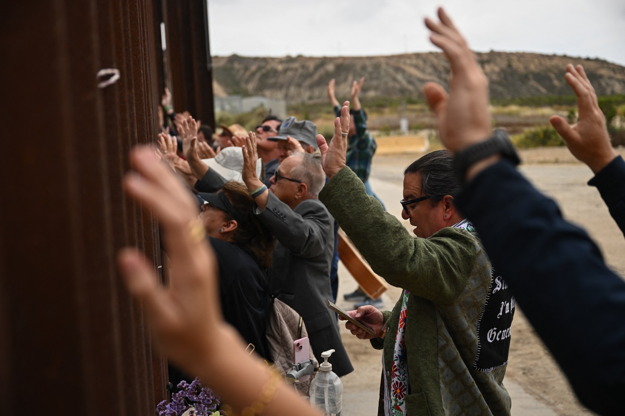 Incoming lead pastor Manuel Retamoza raises his hands in prayer during a service for the Border Church at the stretch of the U.S.-Mexico border fence known as “Whiskey 8” in San Diego on May 25, 2025. The mission of the interdenominational Christian ministry is to maintain presence and “sacramental solidarity” via weekly binational communion services that began in 2011 on both sides of the U.S. and Mexico border. (Photo by PATRICK T. FALLON/AFP via Getty Images)