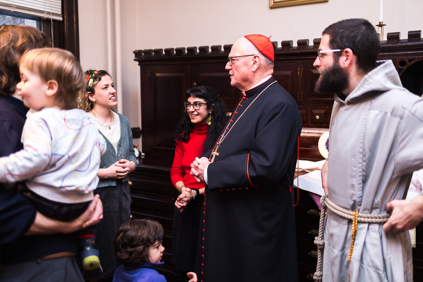 Erin McAtee (left, wearing the colorful headband) and Karina Majewski (right, in the red sweater) chat with Cardinal Timothy Dolan before one of Arthouse 2B's masses for artists in March 2024. (Photo by Edwin Lucero)
